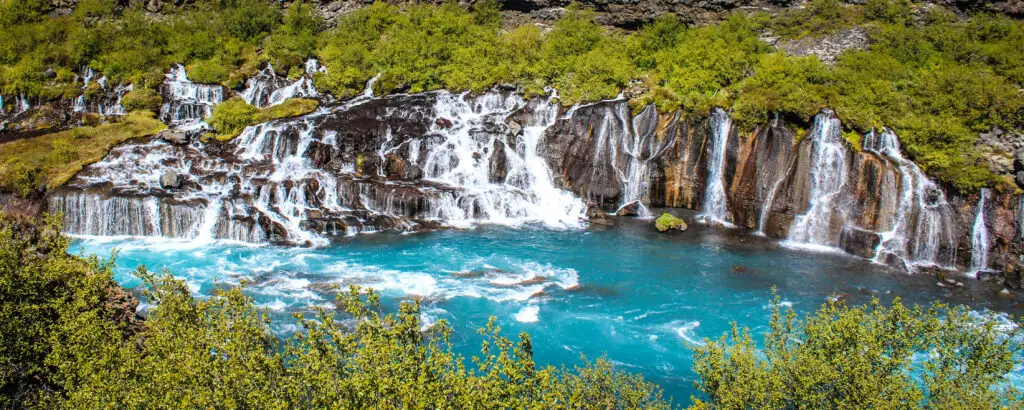 Scenic view of Hraunfossar waterfall in Iceland, showcasing cascading turquoise waters over mossy rocks, ideal for nature and travel enthusiasts visiting Scandinavia