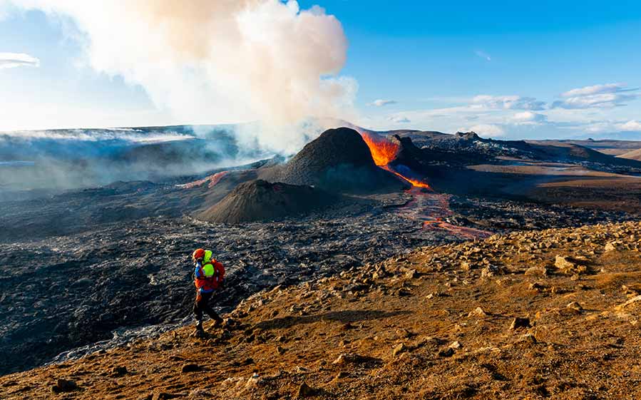 Tourist hiking near active Fagradalsfjall Volcano in Iceland, showcasing flowing lava and smoke against a dramatic landscape.
