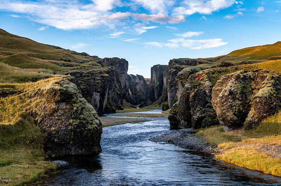 Breathtaking view of Fjaðrárgljúfur Canyon in Iceland, showcasing steep cliffs and a serpentine river flowing through a lush green landscape.