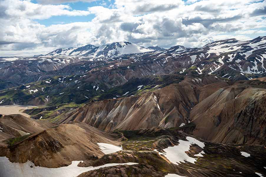 Panoramic view of Fjallabak Nature Reserve in Landmannalaugar, Iceland, showcasing colorful rhyolite mountains and snow patches in a dramatic landscape.