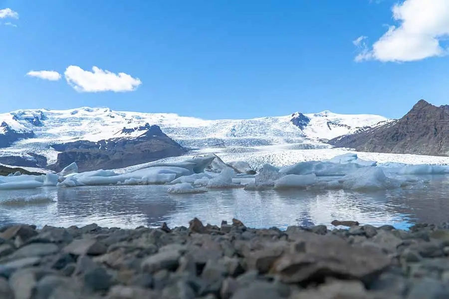Stunning view of Fjallsárlón Glacier Lagoon with floating icebergs and snow-covered mountains in Iceland, a top destination for scenic tours and nature exploration.