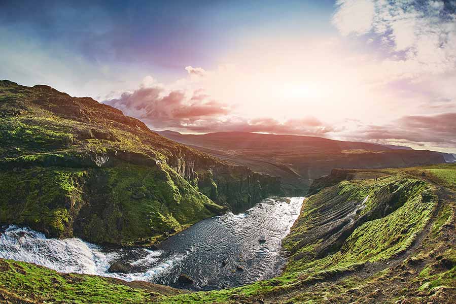 Breathtaking view of Glymur Waterfall in Iceland, showcasing the cascading waters amid lush green landscapes under a sunlit sky.
