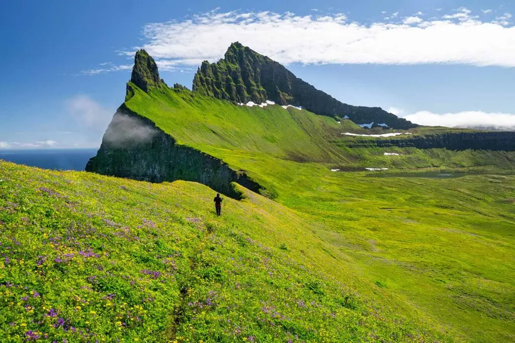 Tourist hiking on the vibrant hillsides of a majestic green mountainous landscape in Iceland, promoting the natural beauty of a 14-day tour in Scandinavia.