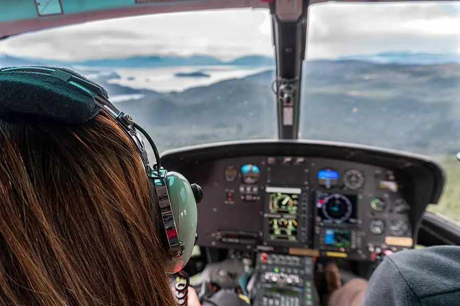 View from inside a helicopter overlooking the scenic landscapes of Iceland, highlighting the cockpit and a pilot wearing headphones focused on navigation.