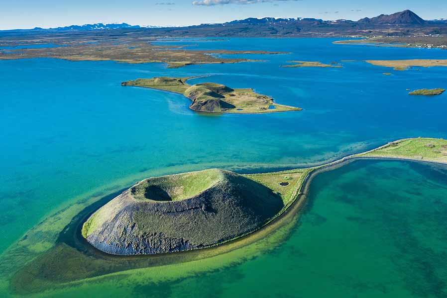 Aerial view of Lake Myvatn in Iceland, showing distinctive volcanic formations and vibrant blue waters surrounded by lush greenery.
