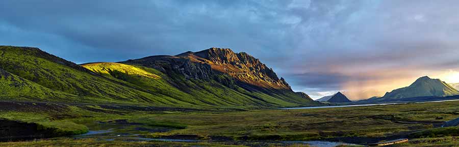 Panoramic view of the stunning Landmannalaugar Valley in Iceland, showcasing vibrant green landscapes and majestic mountains under a soft, glowing sunset.
