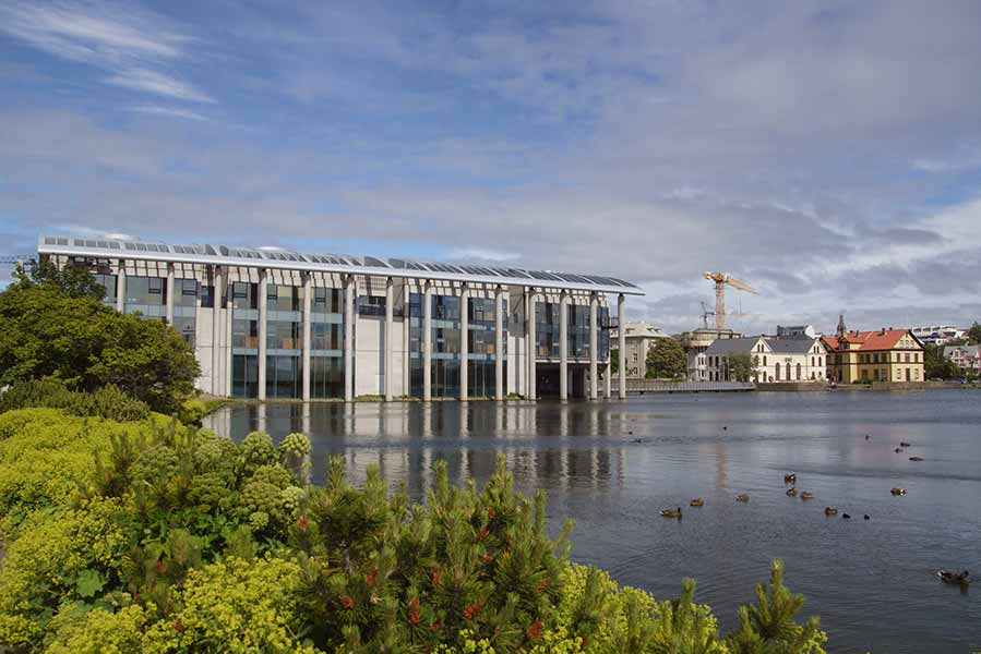 Reykjavík City Hall on the shores of Tjörnin lake, surrounded by lush greenery and architecture in Iceland, on a clear day.