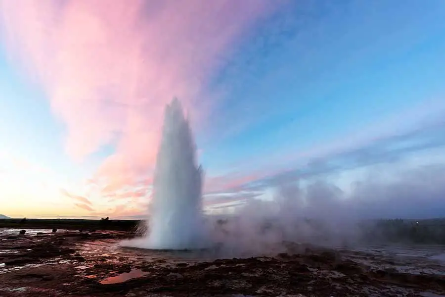 Strokkur Geysir erupting in Iceland with vibrant sky at dusk, a popular Icelandic tourist attraction