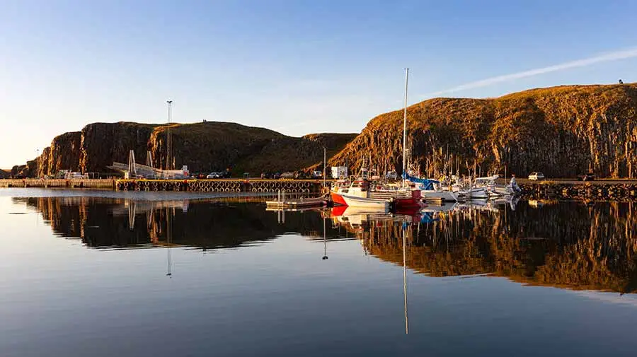 Serene evening at Stykkisholmur Harbor in Iceland with boats reflecting in calm waters surrounded by cliffs.
