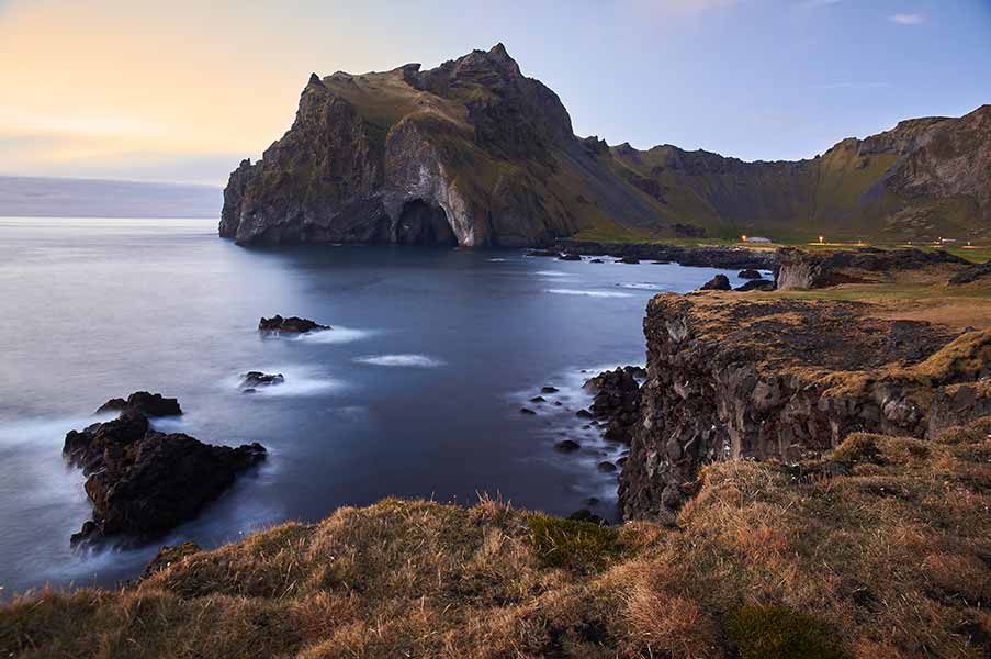 Scenic view of Westman Islands, Iceland featuring majestic cliffs and serene ocean at sunset, ideal for travel and nature enthusiasts.