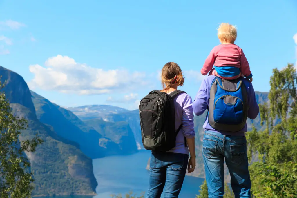 Happy young couple with a small baby enjoying a scenic view of a fjord in Norway, embodying family travel and adventure.