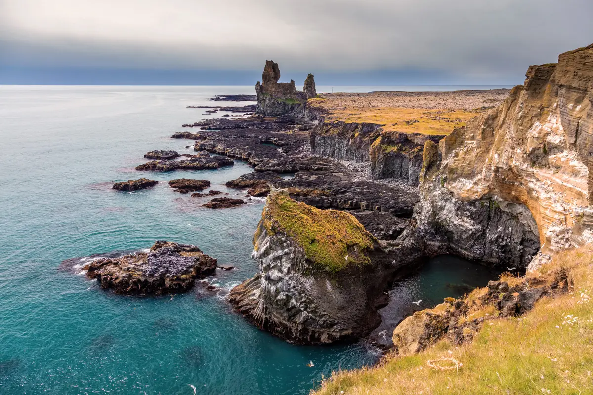 Scenic view of Látrabjarg bird-watching cliffs in the Westfjords of Iceland, showcasing rugged coastline and ocean waves on a cloudy day.