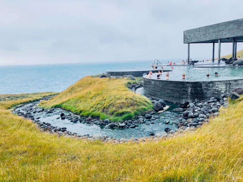 Visitors enjoying the natural GeoSea geothermal swimming pools by the sea in Husavik, Iceland, showcasing beautiful coastal views and sustainable tourist attractions in Scandinavia.