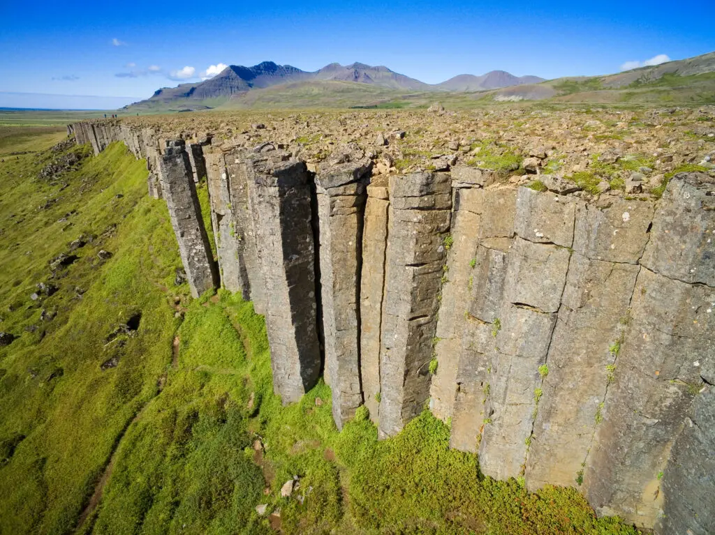 Aerial view of the scenic Gerðuberg Cliffs, a natural basalt column formation on the Snaefellsnes Peninsula in West Iceland, highlighting the rugged landscape and green vegetation.
