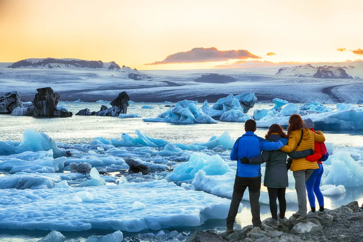 Tourists embracing while observing the stunning sunset over floating icebergs in Jokulsarlon glacier lagoon, Iceland