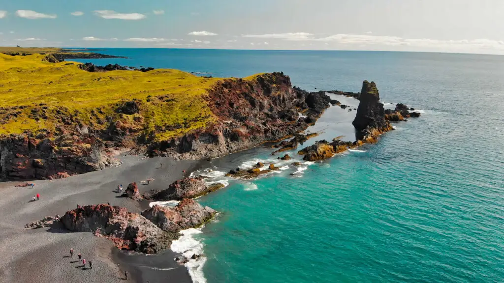 Aerial view of Djupalonssandur coast in Iceland, showcasing the stunning black pebble beach, rugged rock formations, and the vibrant turquoise waters of the North Atlantic Ocean during summer.